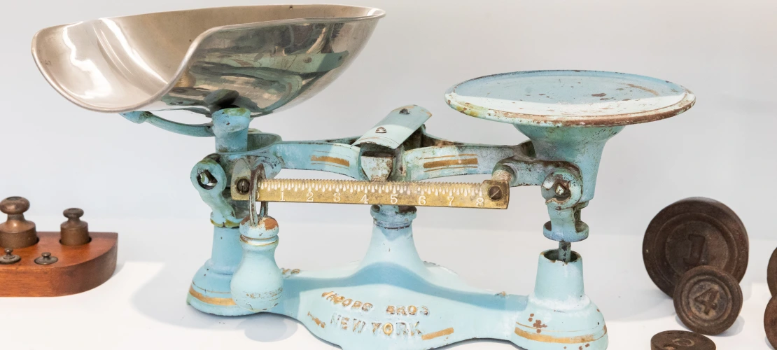 a vintage balance sits on a shelf between brass weights. 