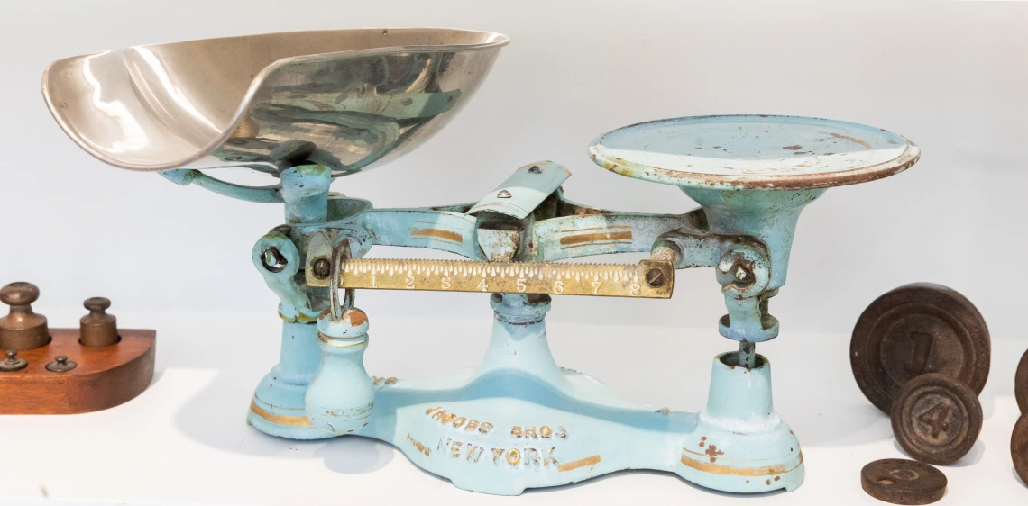 a vintage balance sits on a shelf between brass weights. 